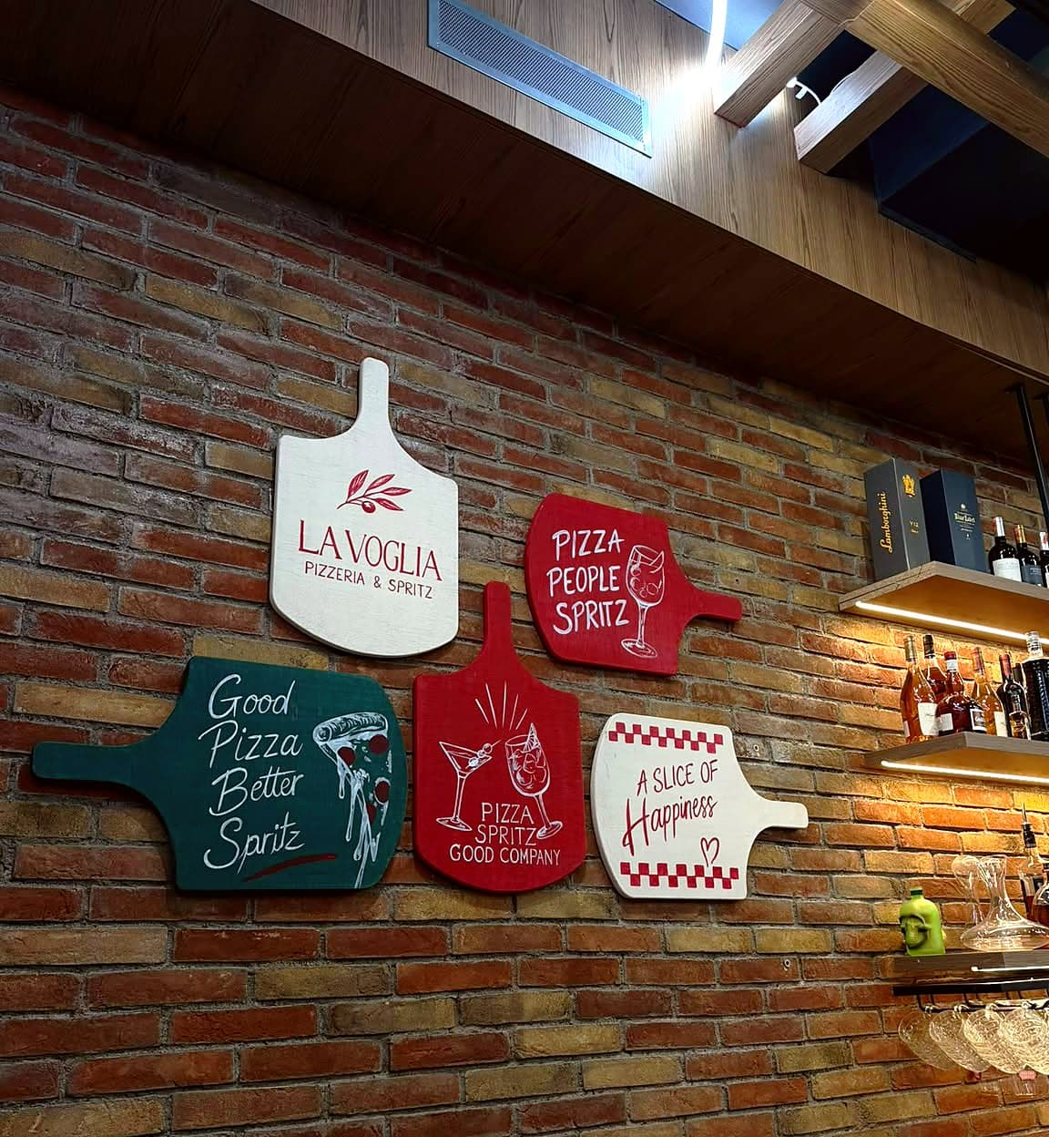 Painted pizza peels on the brick wall: “Good pizza, better spritz”, “Pizza, people, spritz”, “A slice of happiness”